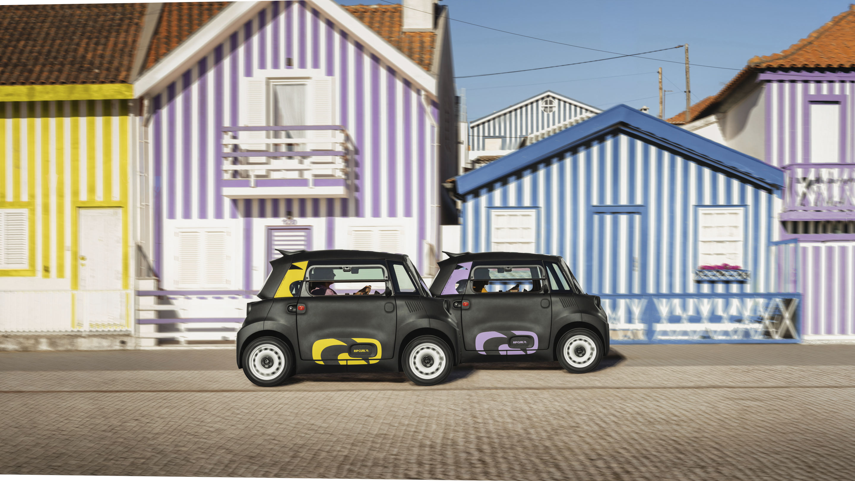 Zijaanzicht van de Citroën Ami x Rip Curl in een stadsstraat: elektrische auto zonder autorijbewijs, met dagelijkse vrijheid voor stedelijke elektrische mobiliteit.