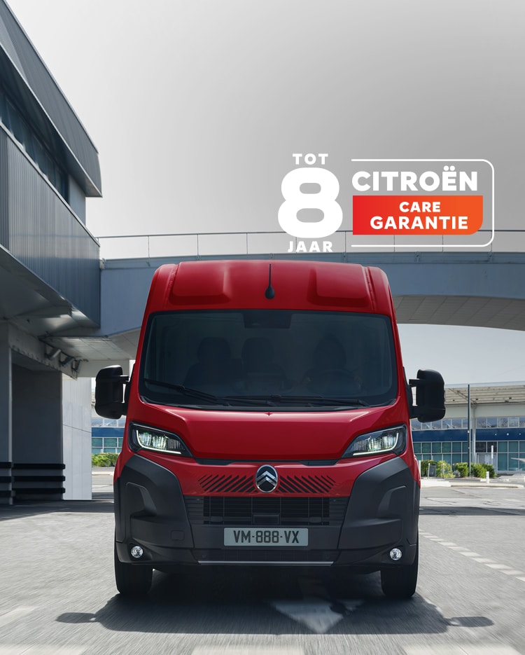 Voorzijde van een rode Citroën Jumper die door een moderne stedelijke omgeving rijdt, waarbij het robuuste ontwerp, het praktische karakter en de krachtige uitstraling worden benadrukt.