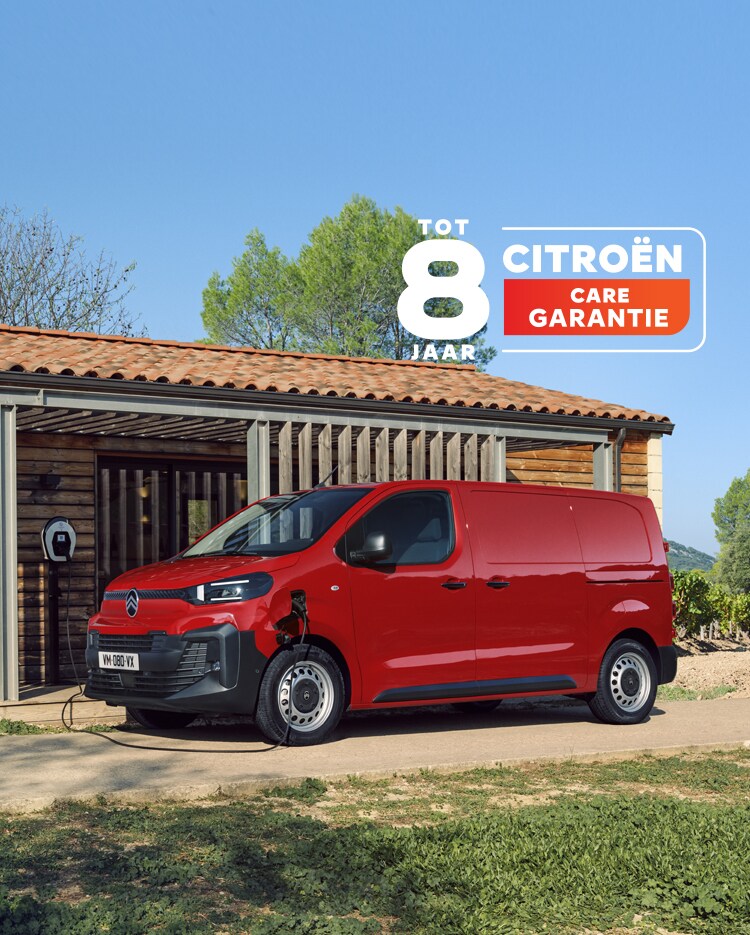 Driekwartsaanzicht van de zijkant van een rode Citroën ë-Jumpy die voor een gebouw wordt opgeladen, waarbij het moderne elektrische ontwerp, de praktische bruikbaarheid voor dagelijks gebruik, de connectiviteit en de zelfverzekerde, professionele uitstraling goed tot uiting komen.